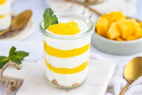Mango-Joghurt-Dessert im Glas geschichtet mit Limettenscheiben und Minzblättern