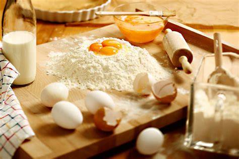 Marillen auf Holzbrett, halbiert, neben Backzutaten (Mehl, Eier, Butter) als Rezept-Infografik