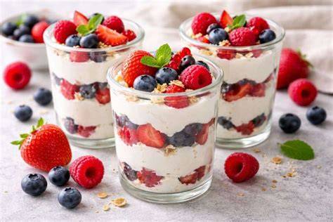 Mehrere Gläser mit geschichtetem Quarkdessert und Beeren, dekoriert mit Minzblättern