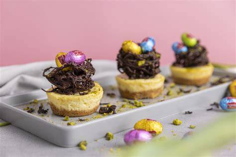 Mini Käsekuchen auf Muffinblech dekoriert mit Schokoladennestern und Pistazien