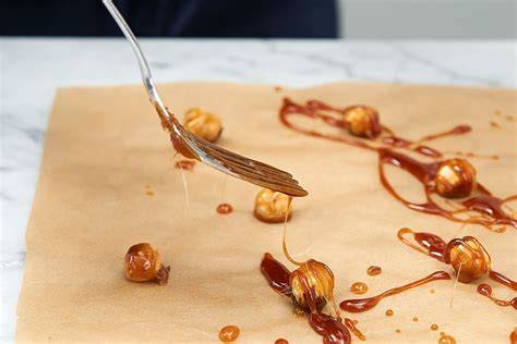 Nuss-Krokant Herstellung: karamellisierte Nüsse auf Backpapier ausrollen