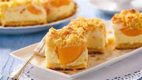 Pfirsich-Schmand-Kuchen mit goldbraunen Streuseln auf Tafel, angeschnittenes Stück