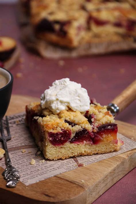 Pflaumenkuchen mit Streuseln auf rustikalem Holzbrett, angeschnittenes Stück, Sahne daneben