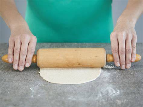 Plätzchenausstecher und Teigrolle auf bemehlter Arbeitsfläche