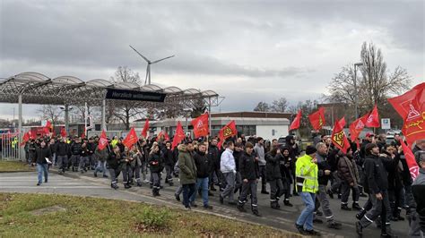 Porträts von Mitarbeitenden und Gewerkschaftsbannern vor dem Werktor