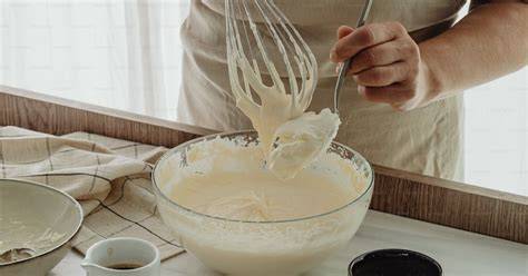 Puddingkochen im Topf, Schneebesen und Schüssel mit Frischhaltefolie