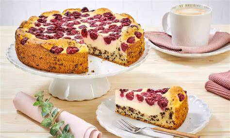 Quark Kirsch Kuchen angeschnitten auf weißem Teller, daneben verschiedene Obstsorten