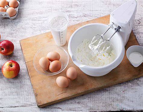 Rühren der Quarkmasse im Handmixer, daneben Marmeladenglas und Eiweißschnee