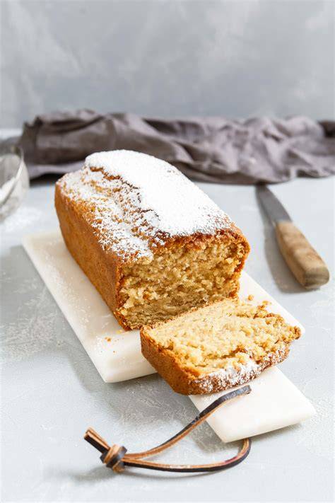 Rührkuchen mit Kokosöl auf weißem Teller, angeschnitten neben Zutaten