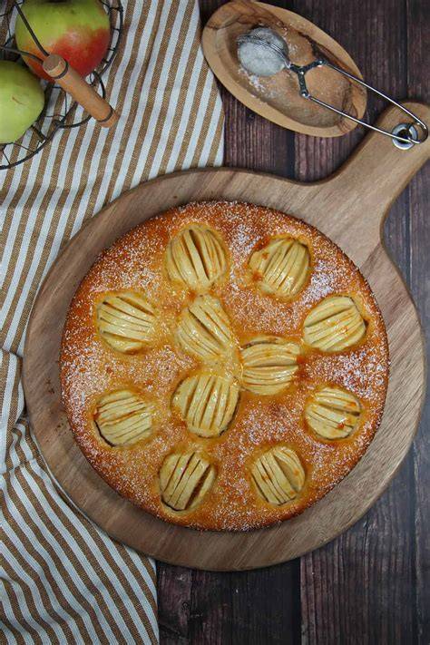 Rustikaler Apfelkuchen auf Holzbrett, aufgeschnittene Äpfel, Zimtstangen