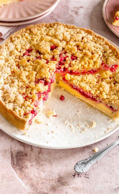 Saftiger Johannisbeerkuchen auf einer Tortenplatte, daneben frische Beeren und Streusel