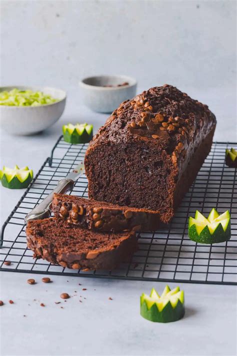 Saftiger Schoko-Zucchini-Kuchen auf Holzbrett, angerichtet mit Schokolade und Zucchinischeiben