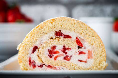 Sahne-Quark-Biskuitrolle mit frischen Erdbeeren, angeschnitten auf einer Sommer-Kaffeetafel