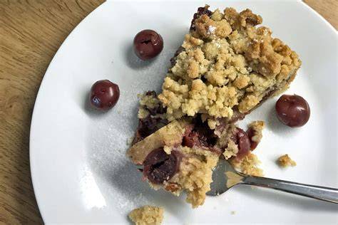 Sauerkirsch Streuselkuchen auf weißem Teller, rustikaler Hintergrund