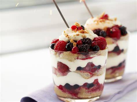 Schichten eines klassischen Trifle im Glas: Biskuit, Pudding, Beeren, Sahne