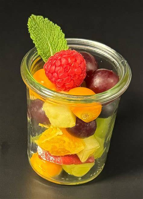 Schichtweise Obstsalat im Glas mit festen Früchten unten und Beeren oben