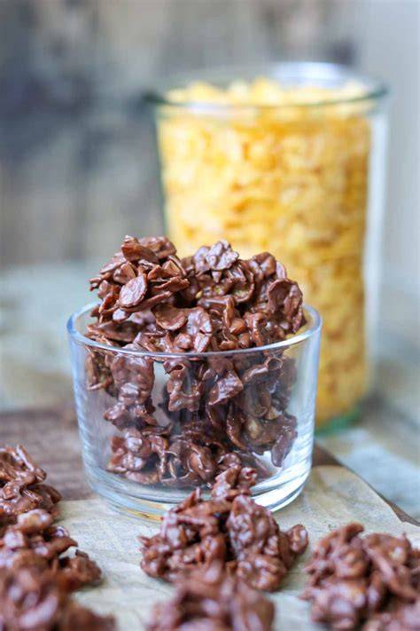 Schoko Crossies neben Zutaten (Schokolade, Cornflakes, Smacks, Mandeln und Gewürze auf Holzbrett)