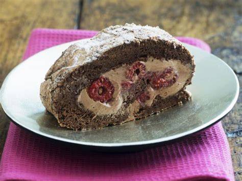 Schoko-Biskuitrolle mit Himbeeren, angerichtet auf einer Tortenplatte mit Schnittbild