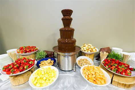 Schokobrunnen auf einem Buffet mit Gästen, die Früchte eintauchen