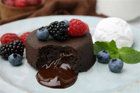 Schokokuchen, angeschnitten mit saftigem Kern, daneben Schlagsahne und Fruchtkompott