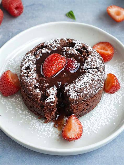 Schokotörtchen mit flüssigem Kern auf Teller, Puderzucker und Beeren
