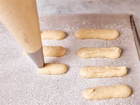 Schritt-für-Schritt-Anleitung mit aufgespritzten Baiser- und Biskuitstreifen auf Backpapier