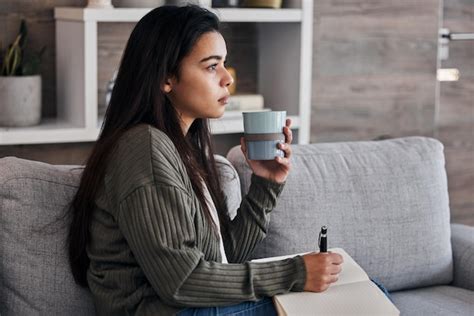Schwangere Frau mit Teetasse und Notizbuch auf dem Sofa