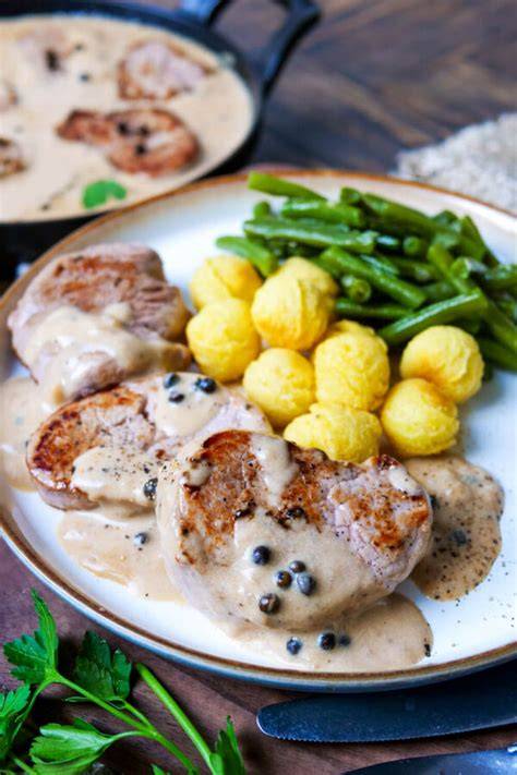 Schweinemedaillons angerichtet mit Honig-Karotten und cremiger Soße auf dem Teller