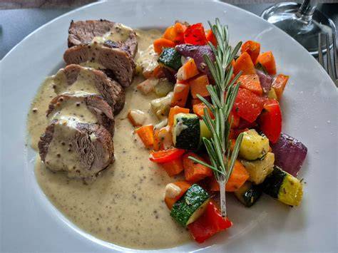 Serviertes Schweinefilet mit Honig-Senf-Sauce auf Ofengemüse