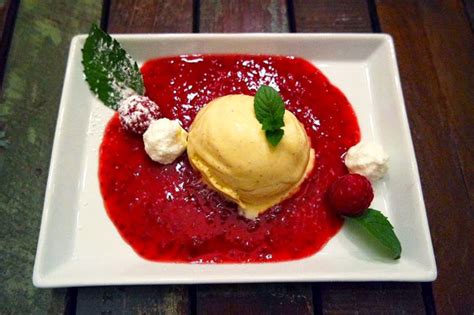 Serviervorschlag: Apfelkuchenstück mit Vanilleeis und Himbeerspiegel, dekoriert mit Zimt