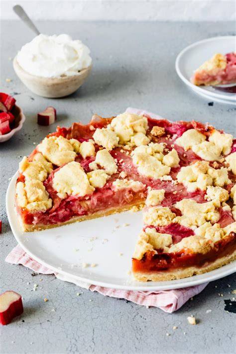 Serviervorschlag: Erdbeer-Rhabarber-Streuselkuchen, angeschnitten, mit Sahne