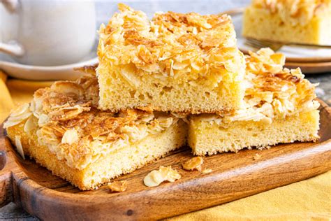 Serviervorschlag: Stück Butterkuchen mit Mandeln, Sahnehäubchen und Kaffee auf rustikalem Holzbrett