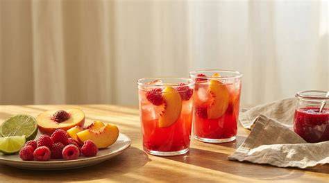 Sommerliche Tafel: Pfirsiche, Himbeeren, Ananas und Limetten neben STAUD’S Gläsern