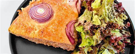 Stück Lachs-Quiche mit Blattsalat auf dem Teller