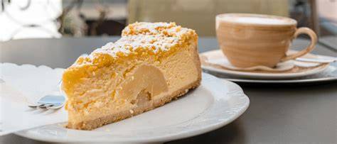 Stück Mascarpone-Apfelkuchen auf einem Teller, daneben Tasse Kaffee