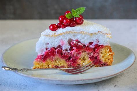 Stück Ribisel Baiser Kuchen auf rustikalem Holzbrett, daneben frische Johannisbeeren