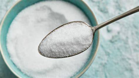 Stevia-Blätter und Erythrit auf einem Löffel neben einer Teetasse