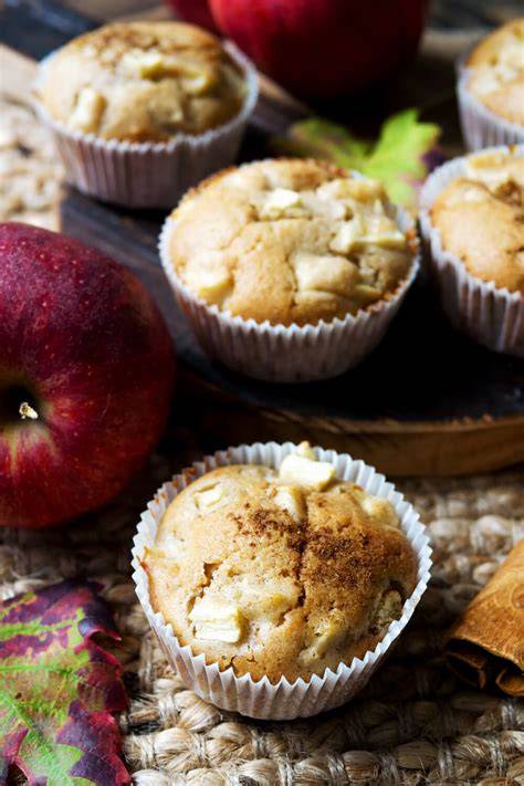 Stimmungsfoto: Gedeckte Apfelmuffins mit Puderzucker, daneben Äpfel, Zimt, Mandeln
