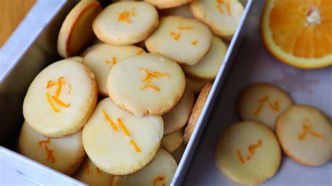Stimmungsvolle Nahaufnahme: Orangenplätzchen auf Blech, Orangeat, Zesten, Pistazien