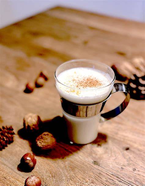Stimmungsvolle Tasse weiße Trinkschokolade mit Zimt und Sahnehaube auf Holztisch