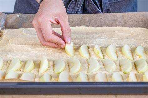 Teig auf dem Backblech mit halb Apfel, halb Pflaume belegt