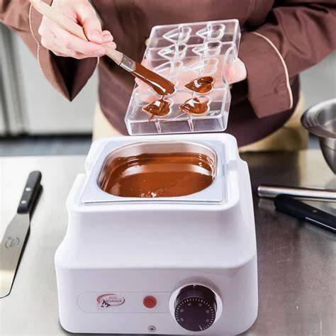 Temperiergerät auf Arbeitsplatte mit Schokolade und Formen