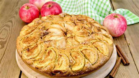 Traditioneller Apfelkuchen auf einer altdeutschen Holzplatte mit frischen Äpfeln und Zimtstangen