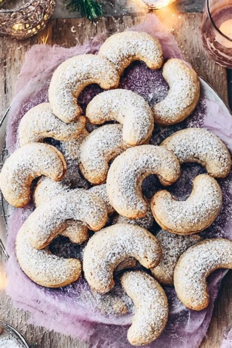Vegane Vanillekipferl auf rustikalem Holzteller arrangiert, dazu einige Mandeln und Vanilleschoten