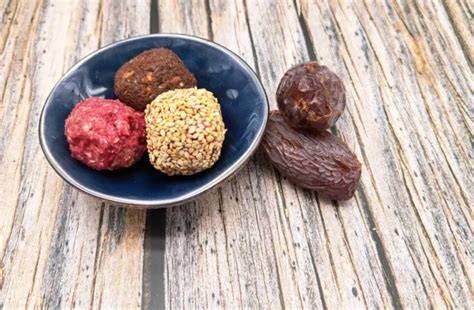 Verschiedene Energy Balls und Dattelpralinen auf einem Holzbrett arrangiert