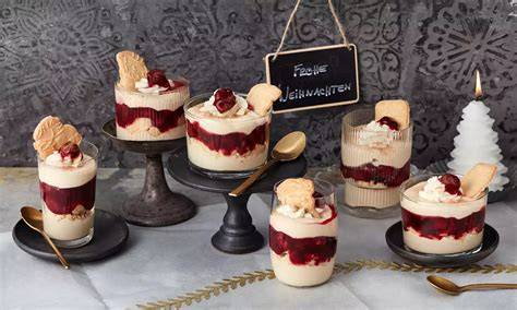Weihnachtliche Dessertgläser mit Spekulatius und Früchten auf festlich gedecktem Tisch