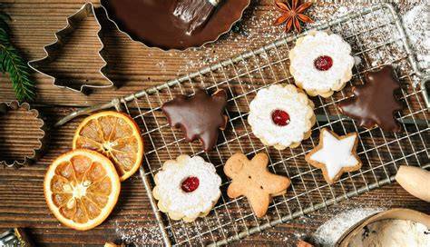 Weihnachtliche Plätzchenvielfalt auf einem Blech, Teig und Ausstechformen im Vordergrund
