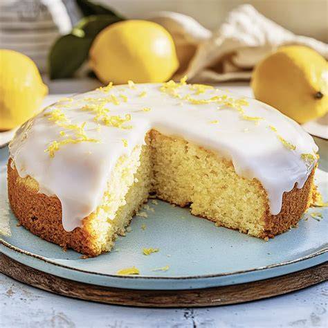 Zitronenkuchen auf einem Teller, angeschnitten, frische Zitronen daneben
