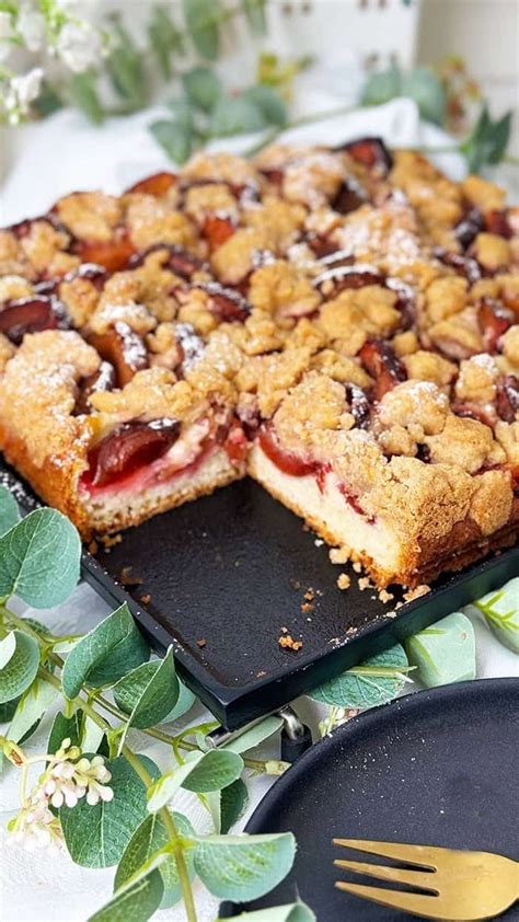Zwetschgen-Blechkuchen mit Zimtstreuseln auf rustikalem Brett, angerichtet mit Sahne