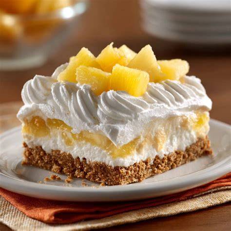 angeschnittener Ananas-Quark-Kuchen ohne Backen auf Glasplatte mit Ananasstücken und Zwiebackrand